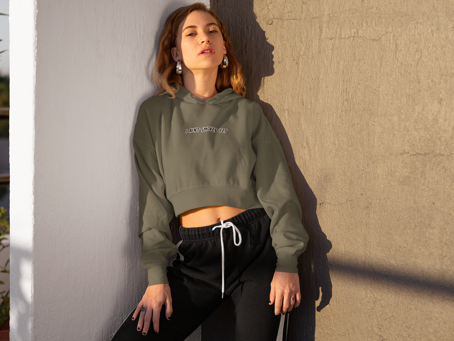 Woman leaning against wall corner. Hoodie says I AIN'T SMOKED YET.