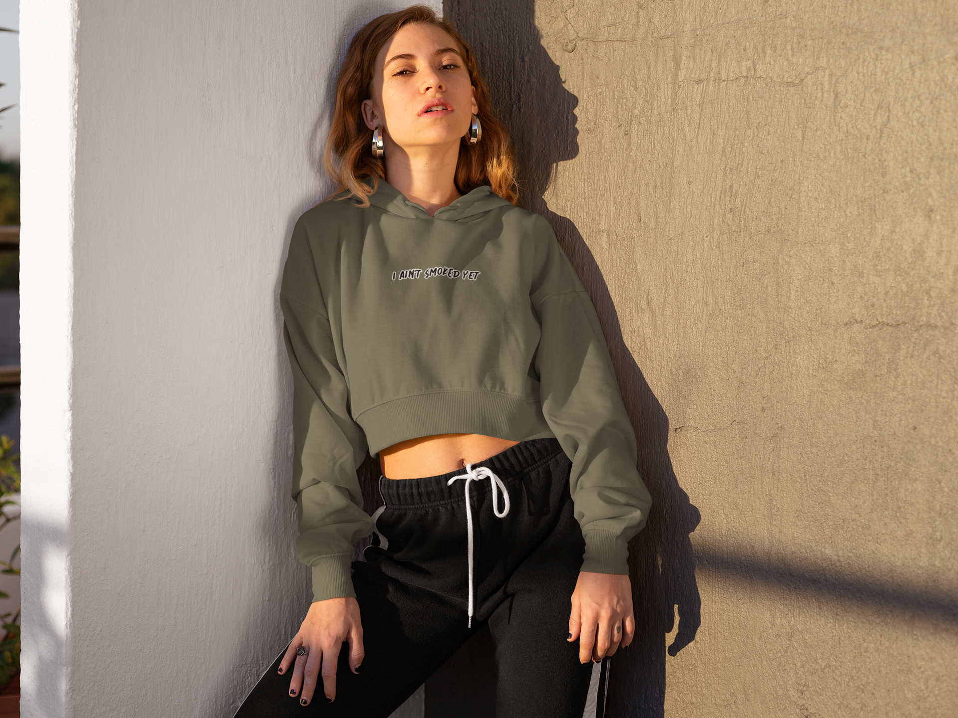 Woman leaning against wall corner. Hoodie says I AIN'T SMOKED YET.